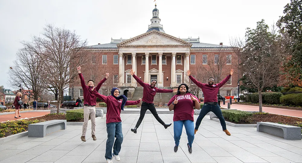 Howard students jumping together in front of a campus building